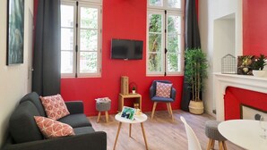 Ein Wohnzimmer mit roter Akzentwand, einem Flachbildfernseher, einem Sofa mit gemusterten Kissen, einem Couchtisch, einem Esstisch mit Stühlen und einem Kamin.