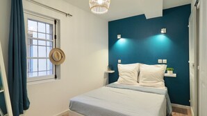 Ein Schlafzimmer mit einem Bett, einem Fenster mit Vorhängen, einem Wandhaken und einer Wandleuchte.