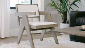 Une pièce comprenant une chaise en bois, une plante en pot, un canapé et une grande fenêtre avec des rideaux blancs.