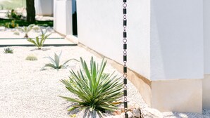 Un bâtiment moderne à l’extérieur blanc, doté d’un luminaire vertical noir et agrémenté d’un jardin aménagé avec des rochers et des plantes.