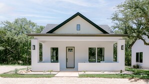 Une maison moderne de plain-pied, avec une façade blanche, un toit foncé et un porche à l’avant.