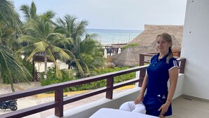Ein Hotelzimmer mit Balkon und Blick auf einen Strand, einem Bett mit weißen Laken sowie einer Aussicht auf Palmen und das Meer.