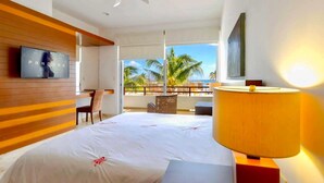 Ein Hotelzimmer mit Bett, Fernseher, Schreibtisch und einem Balkon mit Blick auf Palmen.
