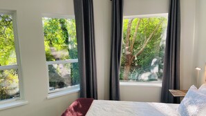 Ein Schlafzimmer mit einem Bett, zwei Fenstern und Blick auf Bäume.