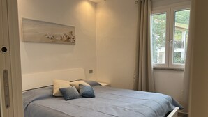 Een slaapkamer met een bed, een raam met gordijnen en een kunstwerk aan de muur.