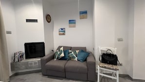 Een woonkamer met een grijze bank, een witte stoel, een zwarte televisie en een wandklok.