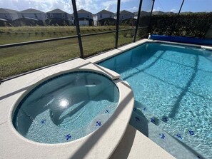 A swimming pool with a hot tub, surrounded by a fence, and houses in the background.