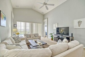 A living room with a sofa set, a coffee table, a flat-screen TV, and a ceiling fan.