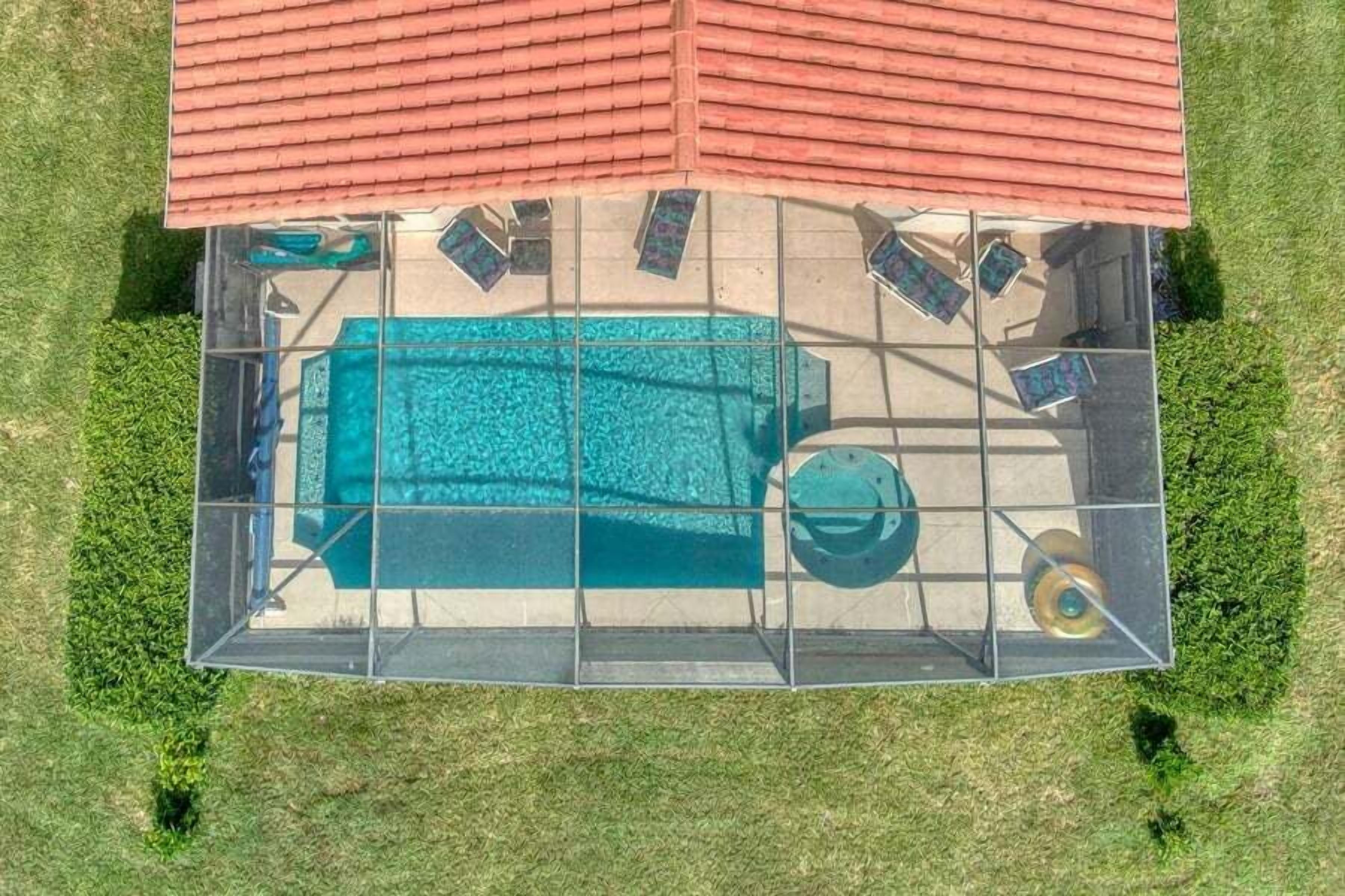 Une vue aérienne d’une piscine dotée d’un toit rouge, entourée d’une structure en verre, et d’un petit espace de détente circulaire.