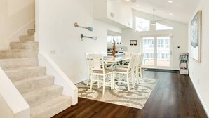 A spacious living area with a dining table and chairs, a staircase, and a ceiling fan. - Seas the Day - Penthouse-like views Gulf, Beach & Bay! (Galveston)