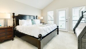 A bedroom with a large bed, two bedside tables, and a staircase leading to an upper level. - Seas the Day - Penthouse-like views Gulf, Beach & Bay! (Galveston)