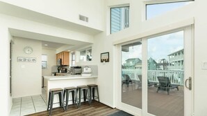 A modern kitchen with a central island, bar stools, and a view of the outdoor deck. - Seas the Day - Penthouse-like views Gulf, Beach & Bay! (Galveston)