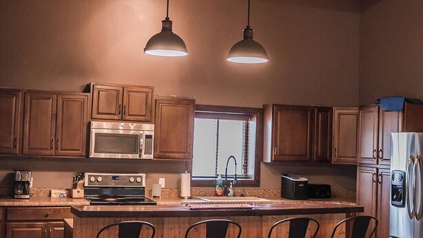 A kitchen with wooden cabinets, a stainless steel refrigerator, a large island with bar stools, and pendant lighting. - Country Lodge (Great Bend)