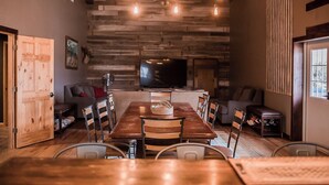 A dining area with a wooden table and chairs, a television on the wall, and a rustic wooden wall. - Country Lodge (Great Bend)