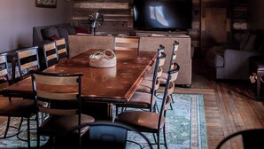 A rustic interior with a wooden ceiling, a dining table with chairs, a sofa, and a television. - Country Lodge (Great Bend)