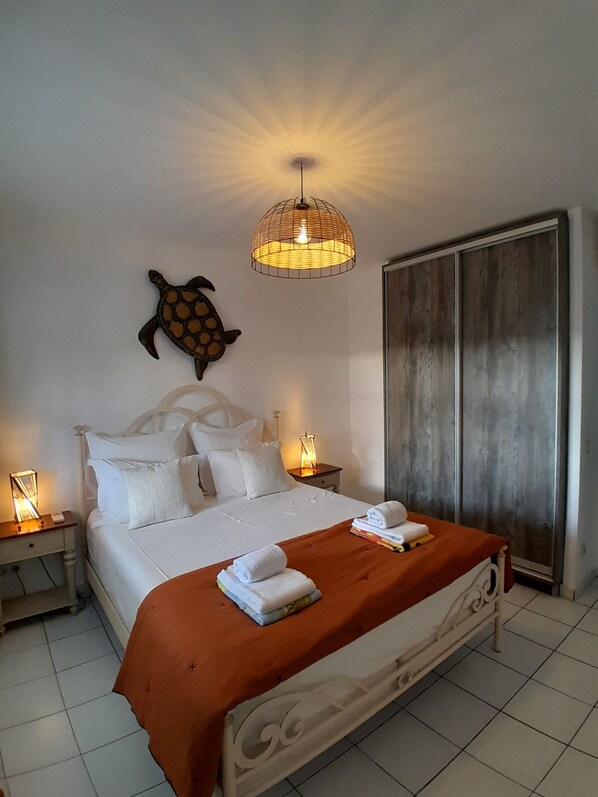 A hotel room with a bed, a nightstand, a wall-mounted turtle decoration, a wardrobe, and a hanging light fixture. - MAGNIFICENT T4, overlooking the lagoon of St François (st françois)