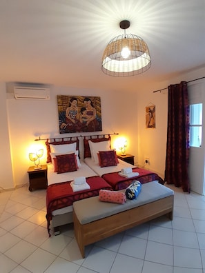 Une chambre d’hôtel avec un lit, des lampes de chevet, un banc et des œuvres d’art accrochées aux murs.