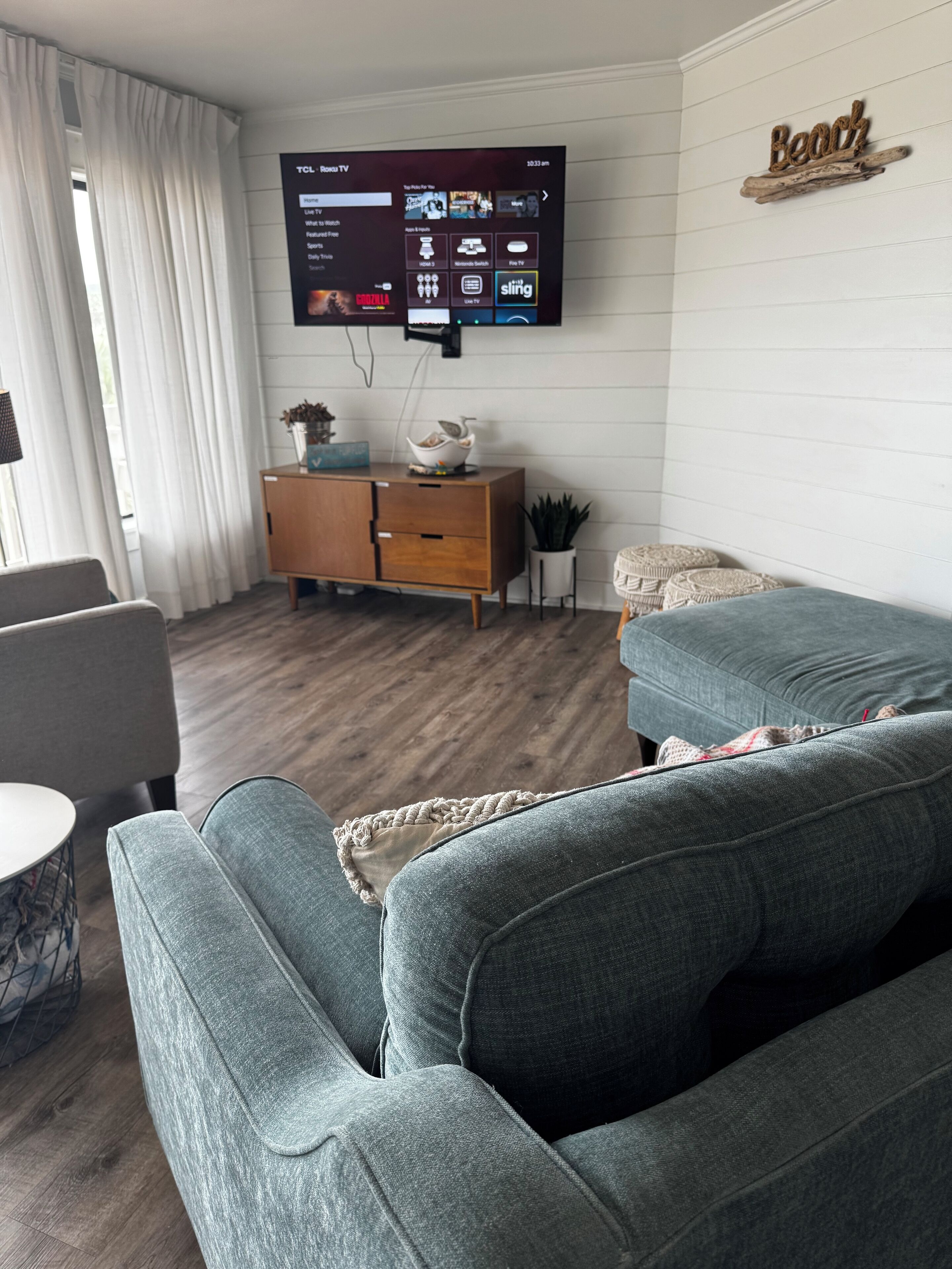 Ein modernes Wohnzimmer mit grauem Sofa, Holzschrank und einem montierten Fernseher, der eine Streaming-Oberfläche zeigt.