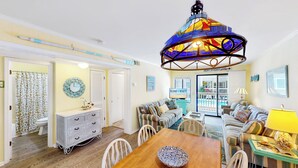 A cozy living room with a dining area, a colorful stained glass ceiling light, and a view of the pool through the glass door.
