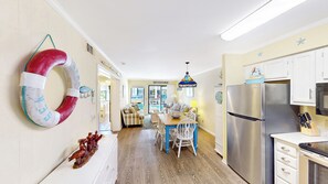A kitchen with a stainless steel refrigerator, wooden flooring, and a dining area with a table and chairs.