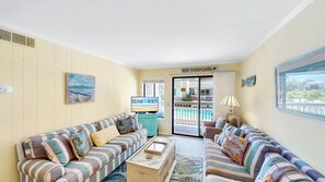 A living room with striped sofas, a television, a painting, and a view of a pool.