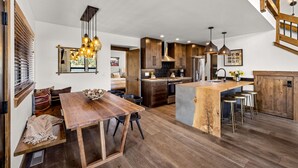 A modern kitchen with wooden cabinets, a central island with stools, pendant lighting, and a view of the living area.