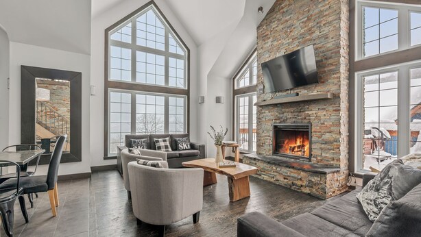 A spacious living room with a fireplace, large windows, and a modern design. - 14- Cottage for rent in Stoneham  (CITQ: 245486) (Stoneham-et-Tewkesbury)