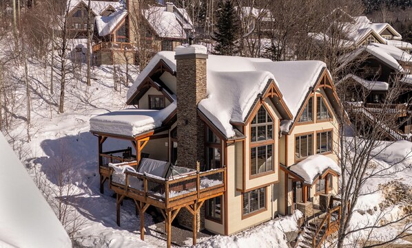 A large, multi-story lodge with a prominent stone chimney, wooden balconies, and snow-covered roofs. - 14- Cottage for rent in Stoneham (CITQ: 245486) (Stoneham-et-Tewkesbury)