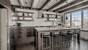 A modern kitchen with a central island, bar stools, and a large window offering a view of the outdoors. - 14- Cottage for rent in Stoneham  (CITQ: 245486) (Stoneham-et-Tewkesbury)
