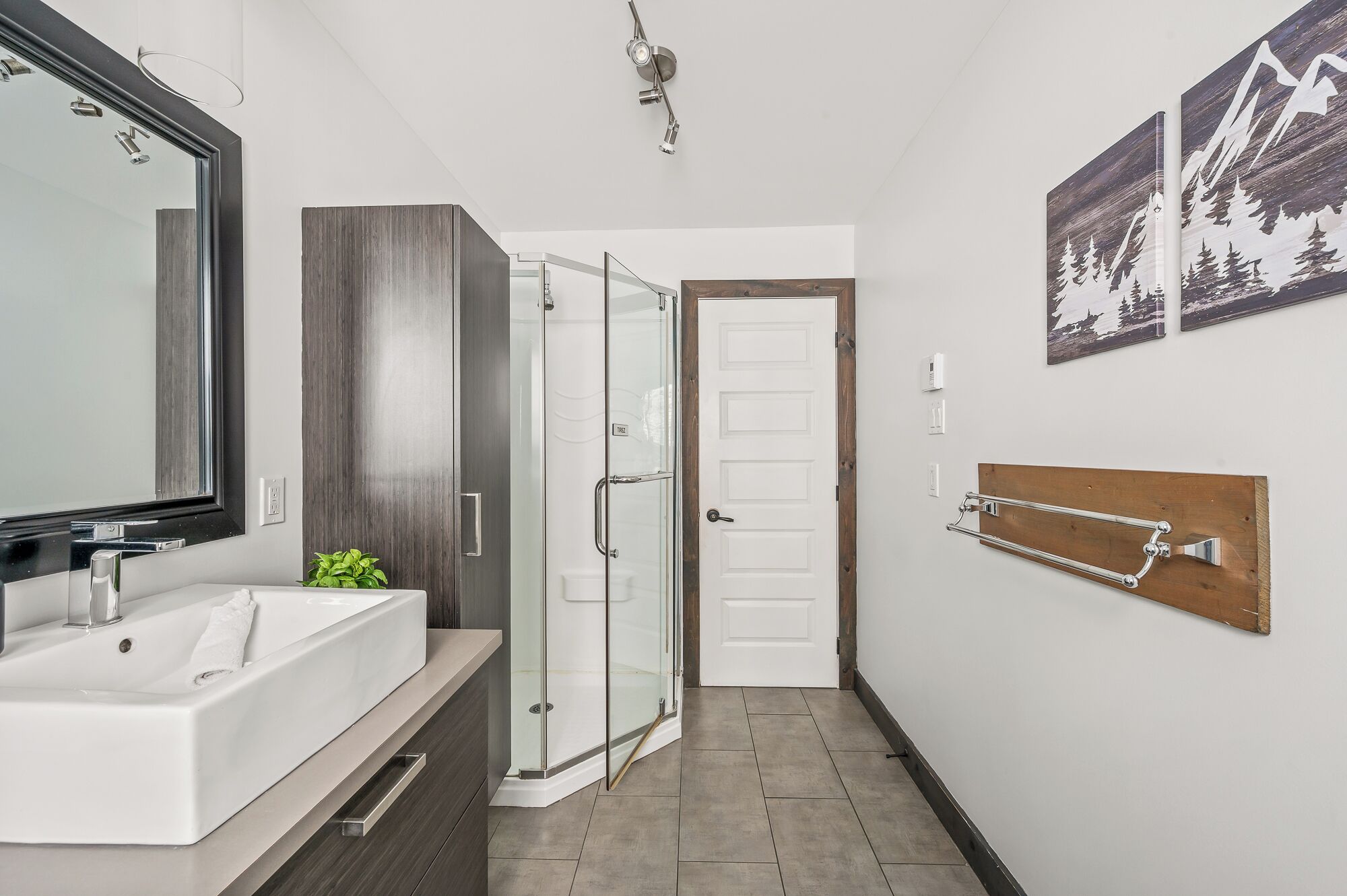 Une salle de bain moderne avec un grand miroir, un lavabo blanc, une douche en verre et une tête de lit en bois.