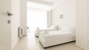 Una habitació d'hotel moderna i minimalista amb dos llits, una zona de seients i una finestra gran.
