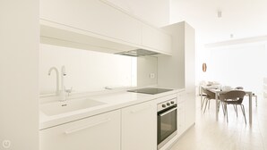 Una cuina moderna amb armaris blancs, forn integrat i zona de dinar amb taula i cadires.