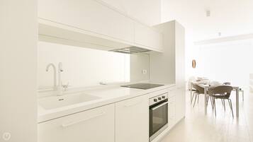 A modern kitchen with white cabinetry, a built-in oven, and a dining area with a table and chairs.