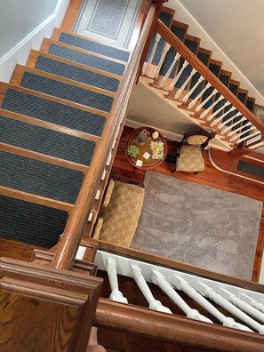 A wooden staircase with a handrail, carpeted steps, and a rug on the landing.