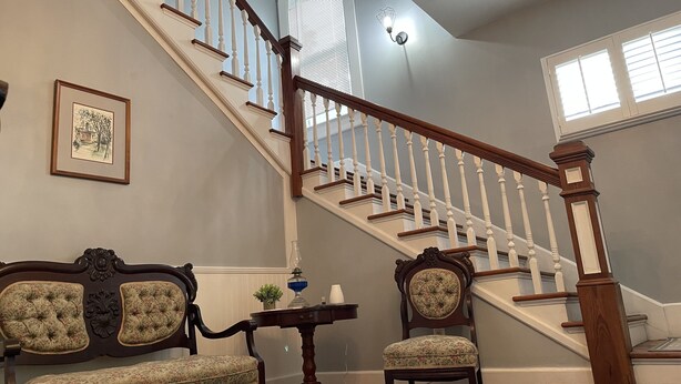 A staircase with white balusters and a wooden handrail, a framed picture on the wall, and a tufted sofa with a floral pattern. - 2/2 Apt downtown in restored historic home yr 1891 (Ocala)