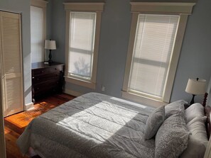 Ein Schlafzimmer mit einem Bett, einer Kommode und zwei Fenstern mit Jalousien.