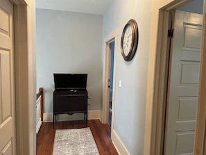 A hallway with a wooden floor, a black cabinet, a rug, and a wall clock. - 2/2 Apt downtown in restored historic home yr 1891 (Ocala)