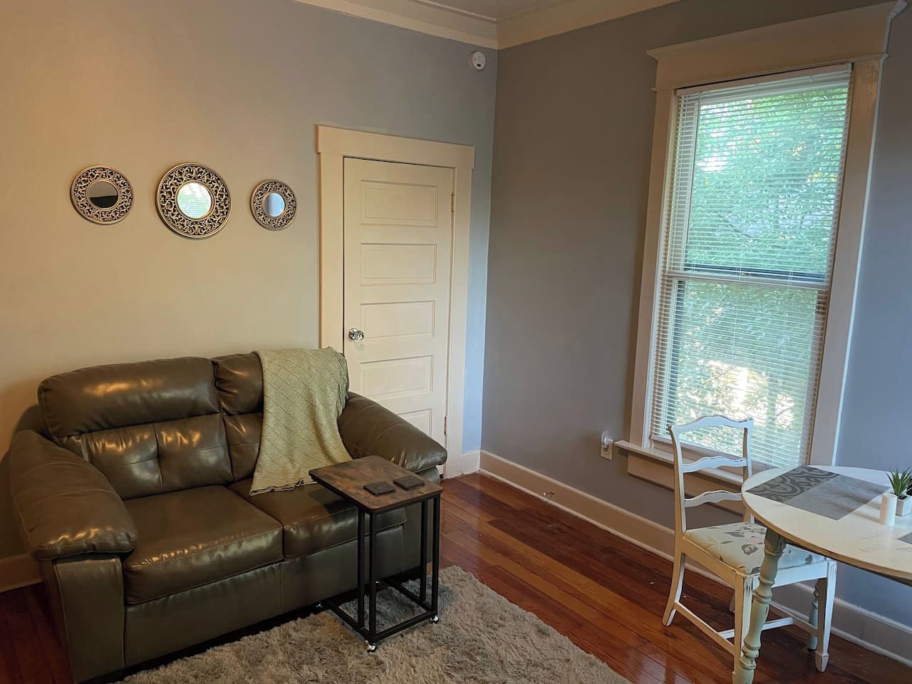 A living room with a leather sofa, a small table, a chair, and a window with blinds.