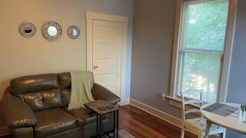 Ein Wohnzimmer mit einer Ledersofa, einem kleinen Tisch, einem Sessel und einem Fenster mit Jalousien.