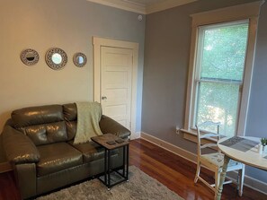 A living room with a leather sofa, a small table, a chair, and a window with blinds.
