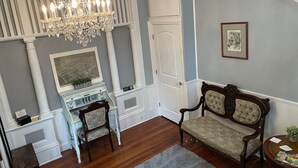 A room with a chandelier, a desk with drawers, two upholstered chairs, a framed picture on the wall, and a wooden floor. - 2/2 Apt downtown in restored historic home yr 1891 (Ocala)