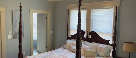 A four-poster bed with a ceiling fan, a bedside table with a lamp, and a window with blinds.