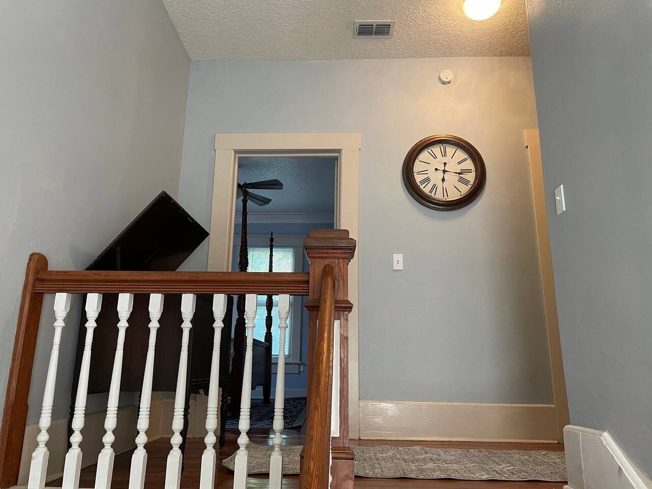 A staircase with a wooden handrail, a wall clock, and a door leading to another room.