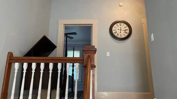 A staircase with a wooden handrail, a wall clock, and a door leading to another room.
