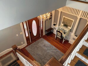 A staircase with a wooden handrail leading to a landing with a grey rug, a chandelier, and a framed picture on the wall. - The Nash House | Historic Downtown Ocala 2/2 (Ocala)
