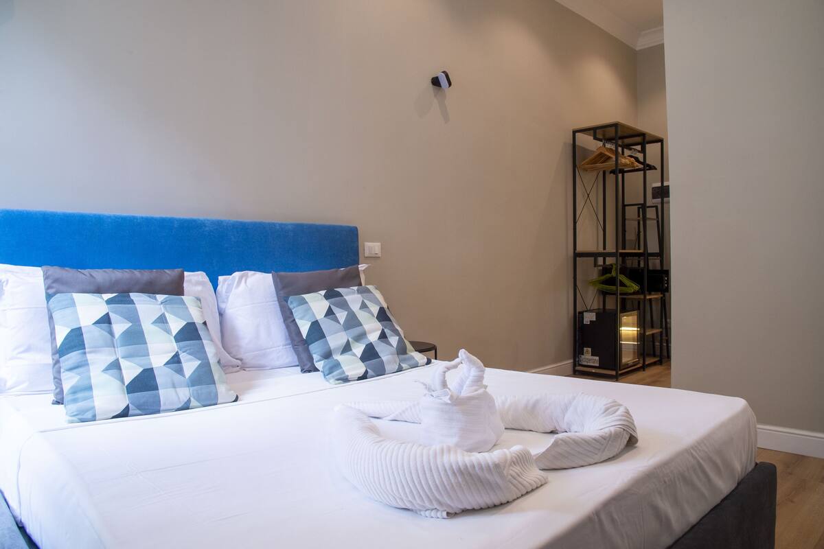 A neatly made bed with geometric patterned pillows, a blue headboard, and a white towel arrangement.