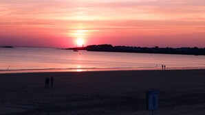 Ranta auringonlaskun aikaan, tyyni vesi ja ihmisten hahmot rannalla.