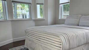 Ein Schlafzimmer mit einem großen Bett, einem gemusterten Teppich und drei Fenstern mit Jalousien.