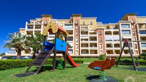 Een speeltuin met een glijbaan en schommels voor een meerlaags hotel met balkons.