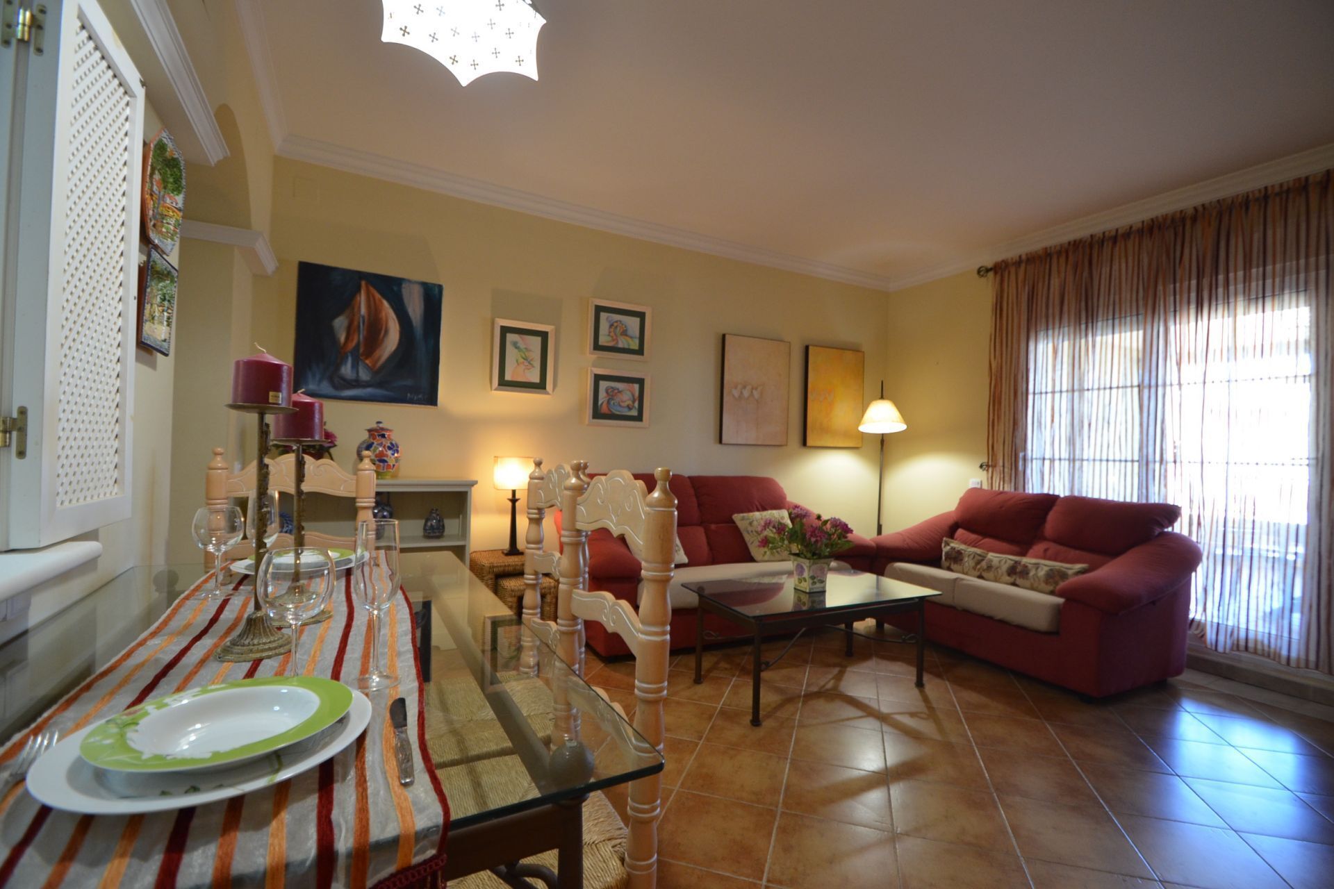 Un salon avec une table à manger dressée pour deux personnes, un canapé rouge et une table basse.